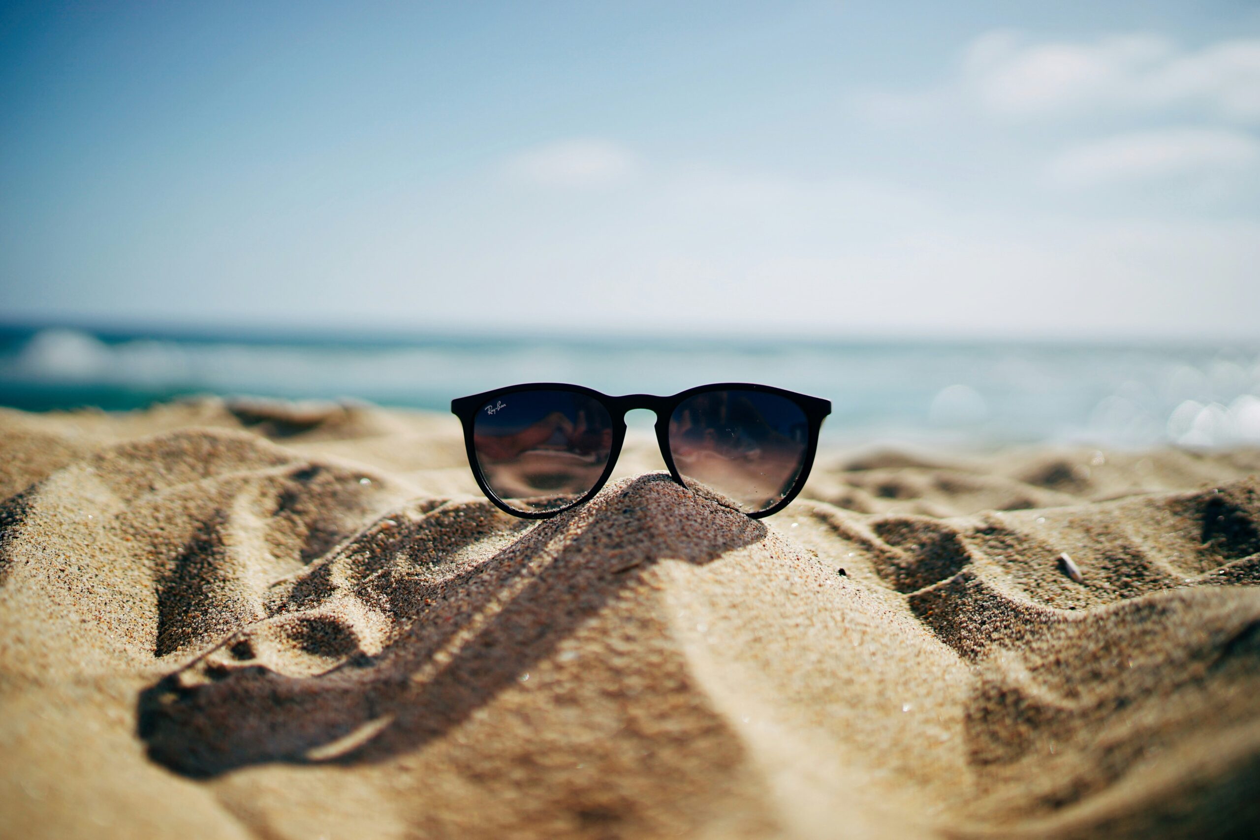 sunglasses sit in the sand on a beach