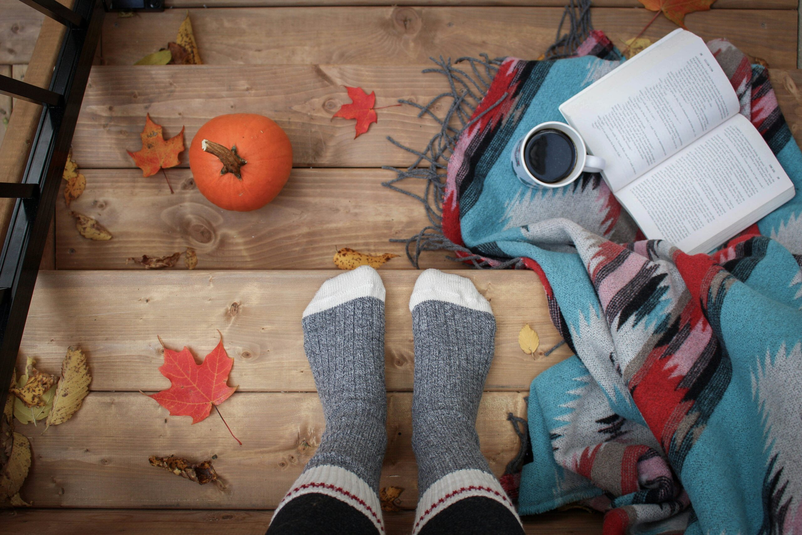 a cozy fall scene with socked feet, pumpkins, and an open book